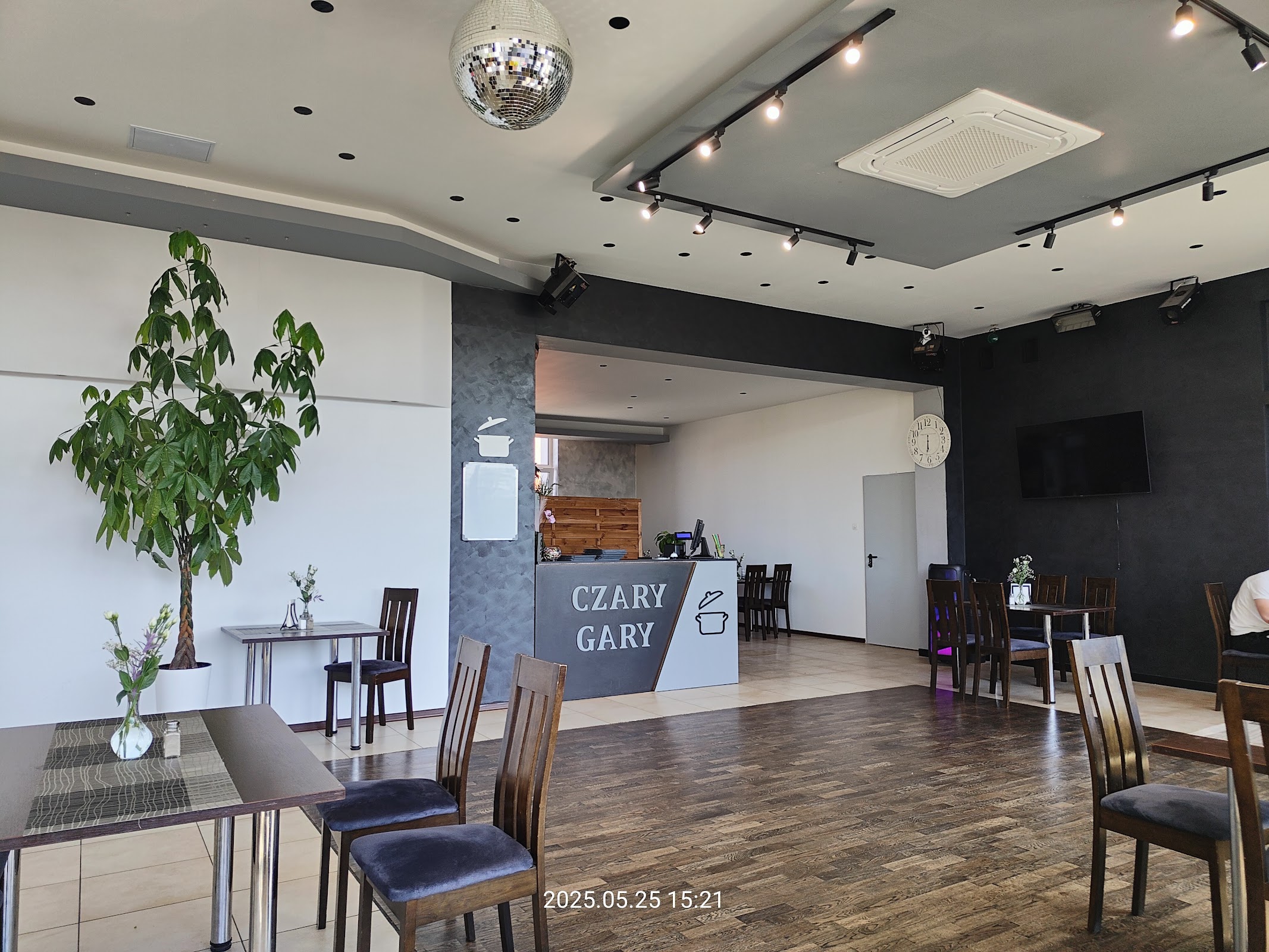 Sala restauracyjna Czary Gary, kula dyskotekowa pod sufitem, czarna ściana z paskiem akustycznym, lada z logotypem w głębi.